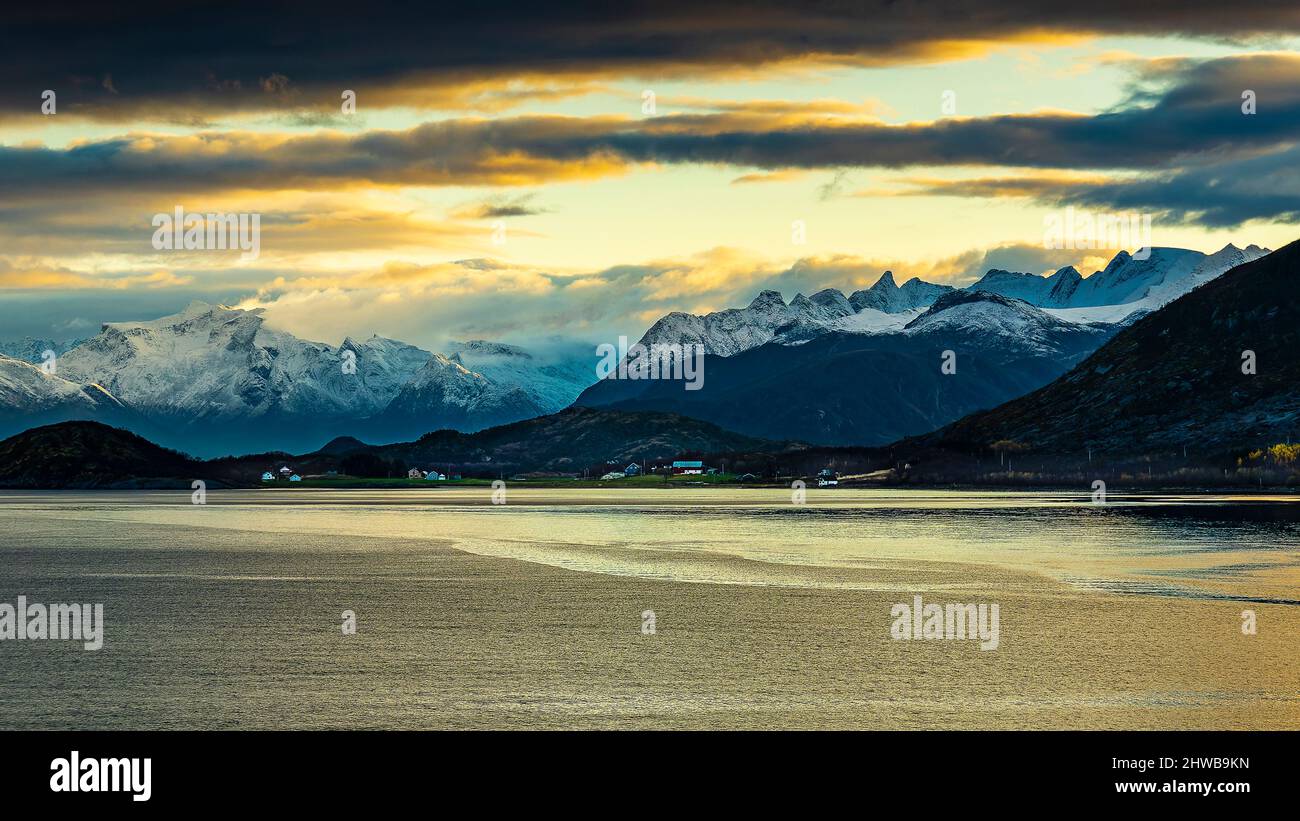 Vom Sonnenaufgang Orange gefärbte Wolken über den frisch verschneiten Bergen der Küste von Norwegen, zwischen Nesna und Ørnes im Nordland. Foto Stock