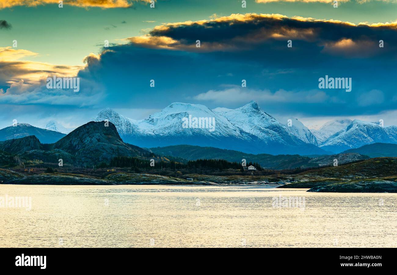 Vom Sonnenaufgang Orange gefärbte Wolken über den frisch verschneiten Bergen der Küste von Norwegen, zwischen Nesna und Ørnes im Nordland. Foto Stock