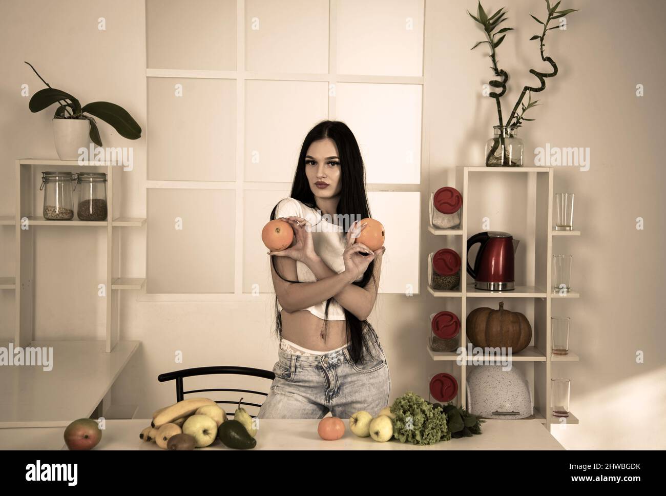 Calzata sportiva che tiene l'arancia vicino a frutta, verdura e metro a nastro su tavola da cucina, dieta per contare le calorie Foto Stock