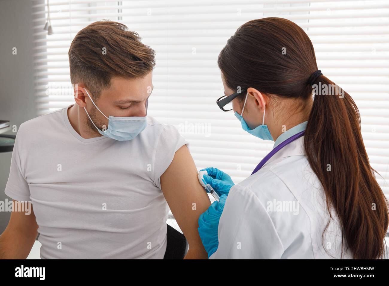 Il medico tiene una siringa prima di fare un'iniezione a un paziente in una maschera medica. Covid-19 o vaccino contro il coronavirus. Vaccinazione della popolazione Foto Stock
