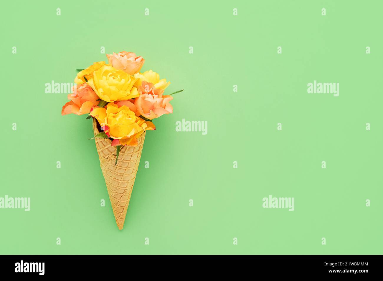 Rose gialle in un cono gelato a cialda su sfondo verde. Festa delle madri, giorno di San Valentino, bachelorette, concetto estivo. Spazio di copia, vista dall'alto Foto Stock