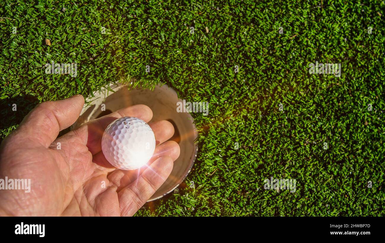 Primo piano da mano con la palla da golf vicino al buco con raggi solari artificiali Foto Stock