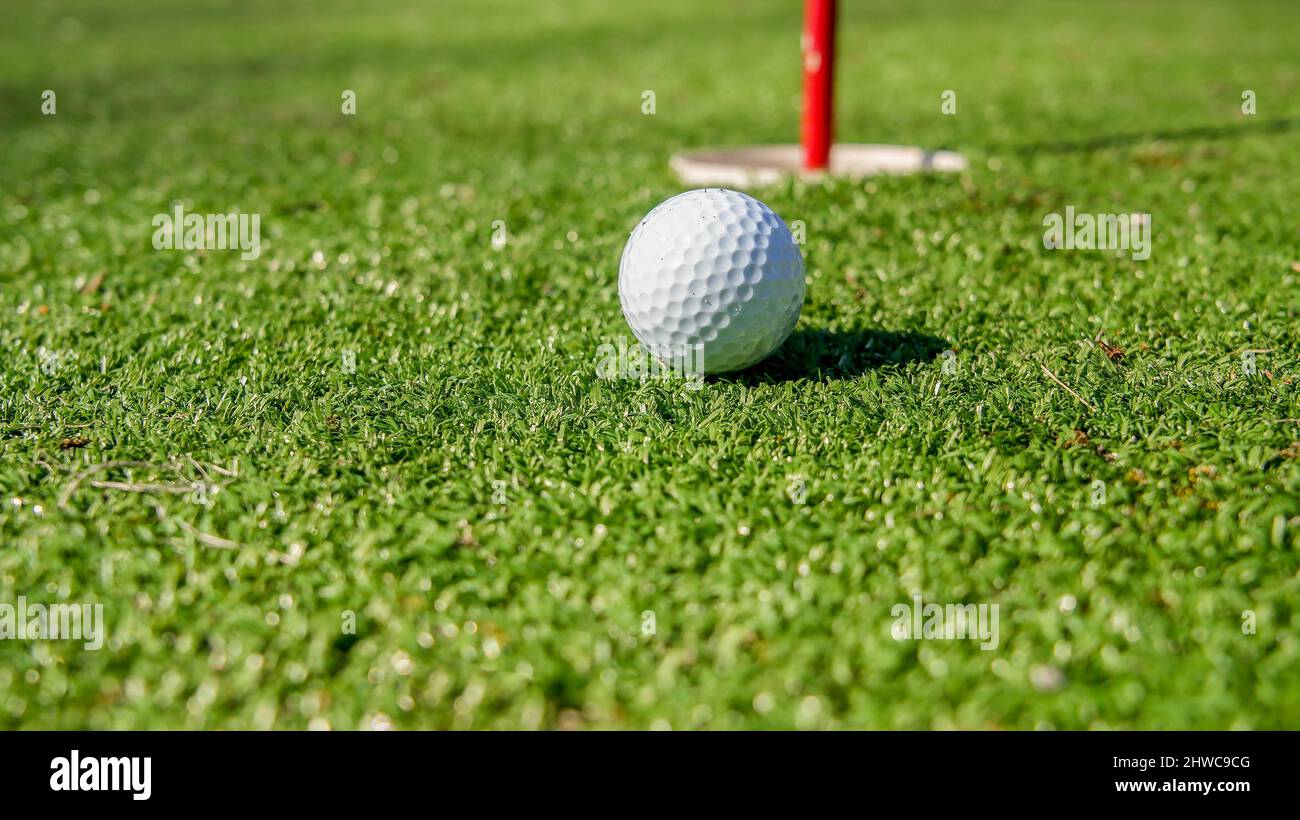 Palla da golf vicino al buco con bandiera sul verde Foto Stock