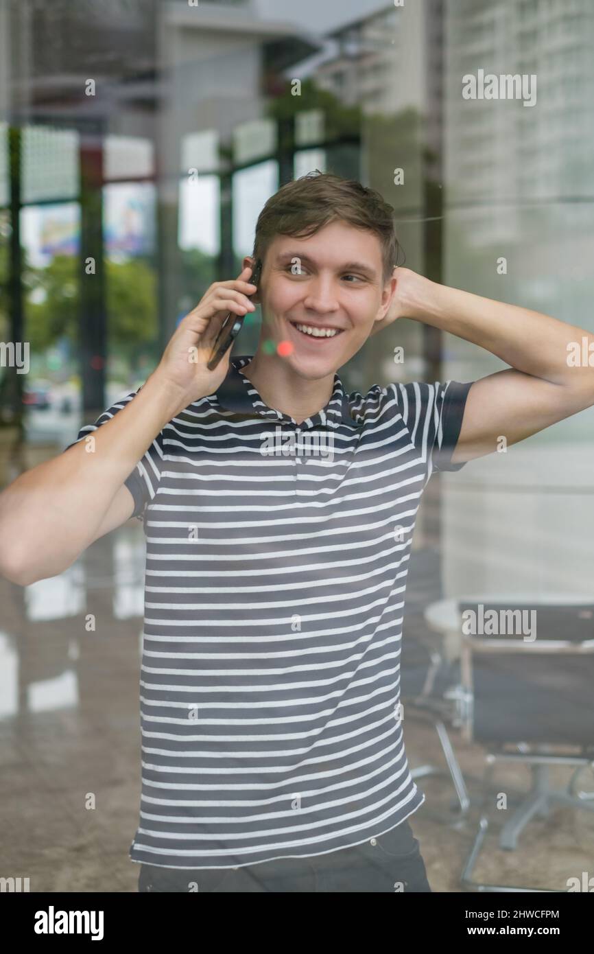Ritratto del giovane uomo caucasico in abiti casual facendo telefonata. Foto attraverso il vetro. Utilizzando lo smartphone, parlando al telefono. Stile di vita urbano. Foto Stock