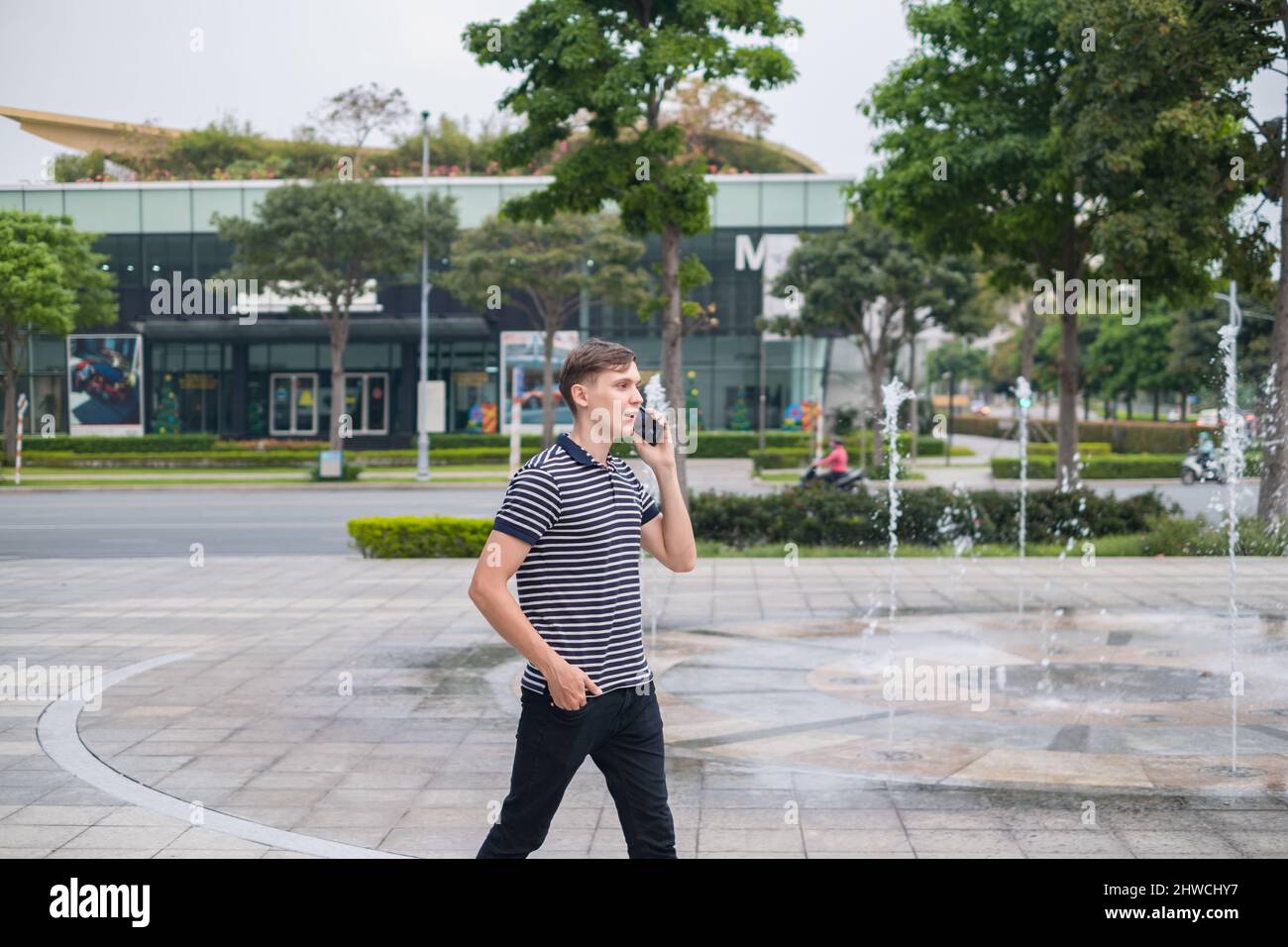 Ritratto del giovane uomo caucasico in abiti casual a piedi all'aperto e fare una telefonata. Utilizzando lo smartphone, parlando al telefono. Stile di vita urbano. Foto Stock