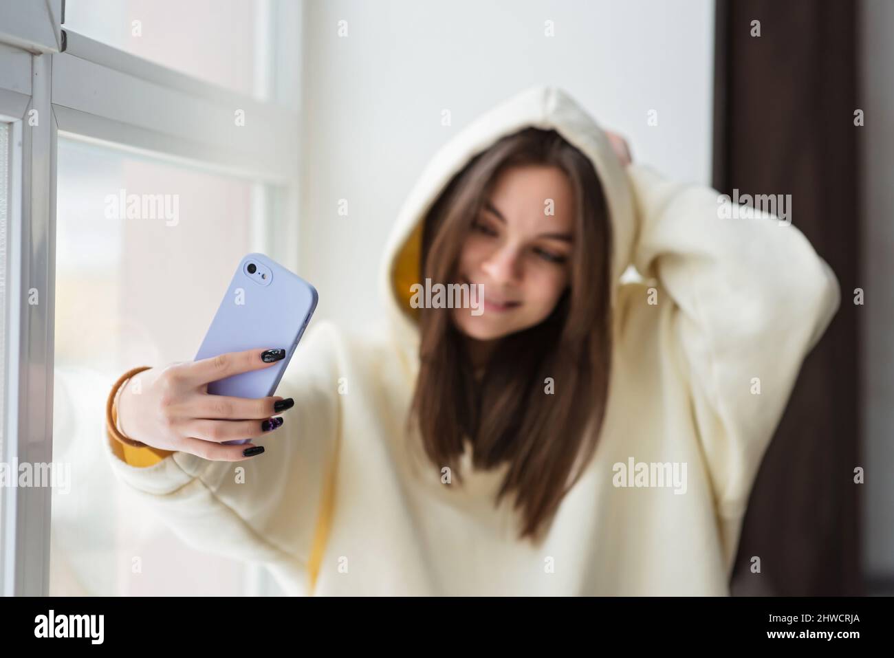 Sorridendo giovane adolescente videochiama sul cellulare, parla con amici, famiglia, porta selfie per i social media, rimani connesso durante la pandemia Foto Stock