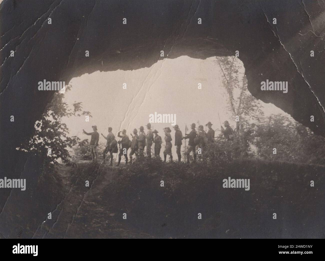 Iconico Archivio storico immagine della silhouette di un gruppo di ragazzi scout i cui caschi sono in erba e si trovano di fronte a una grotta. Questa foto è perfetta. Foto Stock