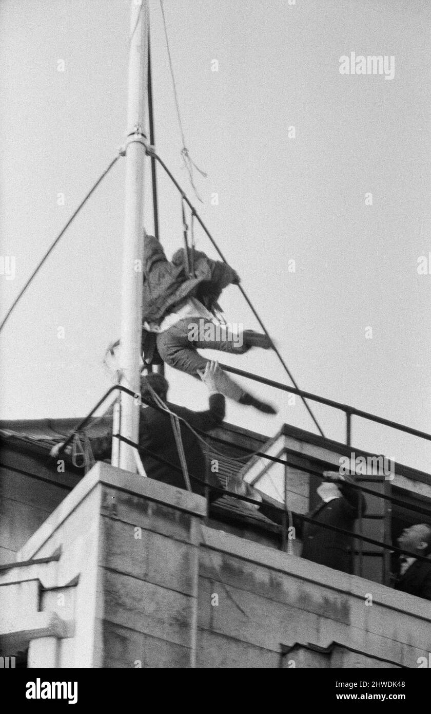 Ann Warren, studente di 22 anni, salì in cima alla casa di Rhodesia, prese la bandiera del regime ribelle smith e la sostituì con Union Jack. Nella foto, mentre Ann scende dal palo della bandiera scivola e quasi cade, i funzionari della Rhodesia House la aiutano a scendere. A 5pm anni prese l'Union Jack giù e finalmente venne sul marciapiede Strand per una conferenza stampa e un bacio dal suo ragazzo, Ian Middlehurst, che era uno dei due uomini che trascorse una domenica arroccato nella stessa posizione all'inizio del mese. 27th gennaio 1969. Foto Stock