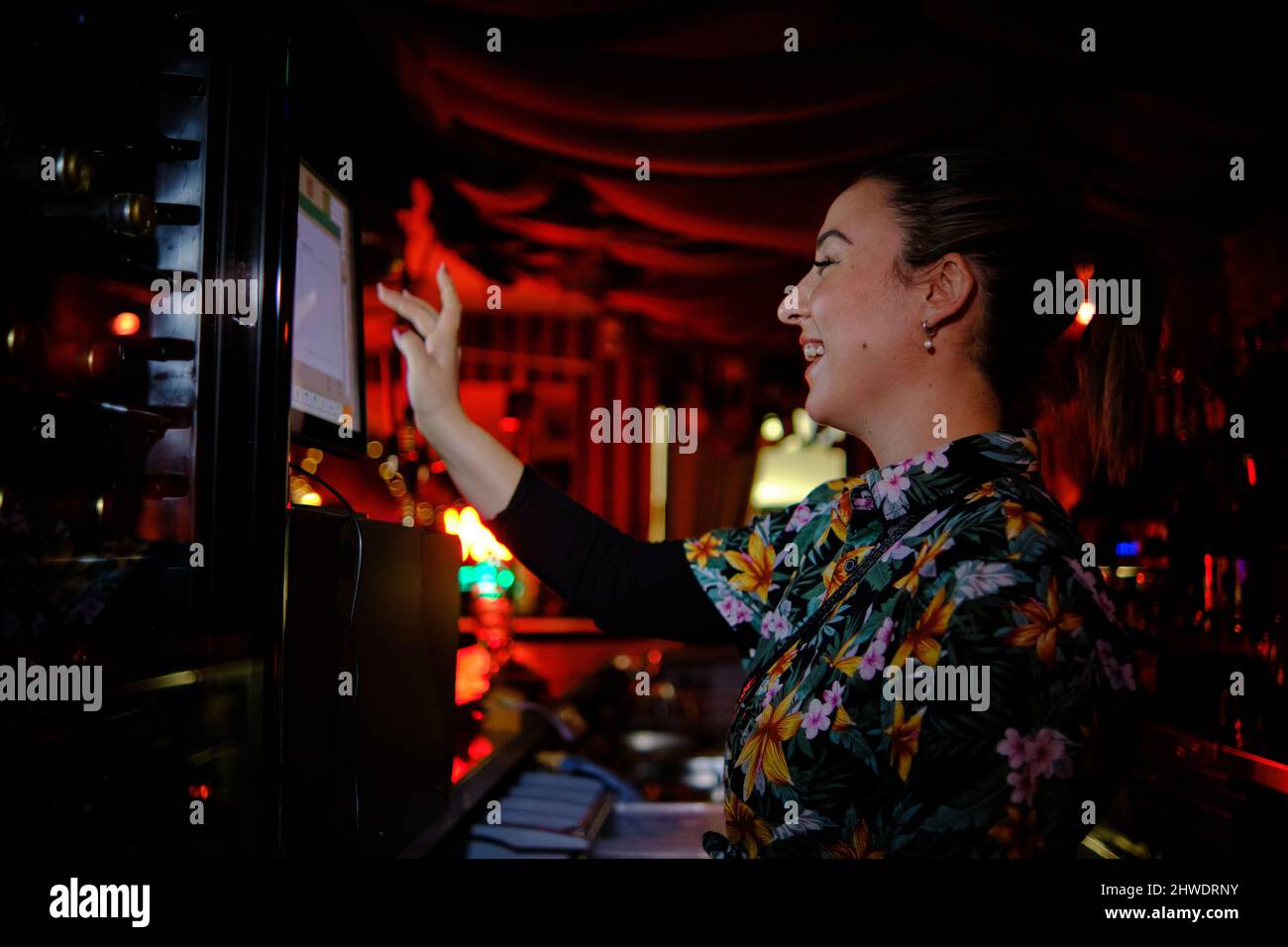 Cameriera femminile che usa un computer touch screen e sorride mentre lavora dietro il bancone in un bar. Foto Stock
