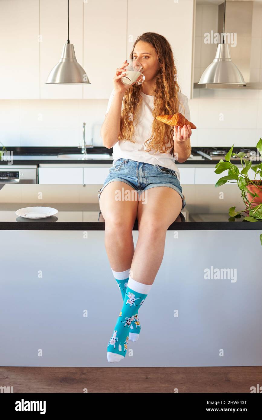 Giovane donna che beve latte in cucina Foto Stock