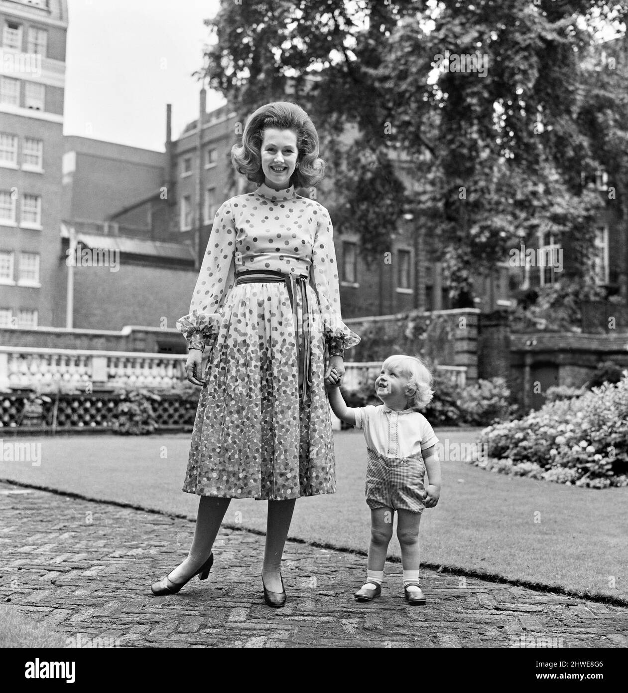 Lady Dartmouth, figlia di Alexander McCorquodale e romantic romanziere Dame Barbara Cartland, ha votato una delle 10 migliori donne di abbigliamento del paese. È raffigurata a casa sua con un abito midi multicolore, con il suo figlio di 20 mesi Henry Legge - il suo quarto bambino. 21st settembre 1970. Foto Stock