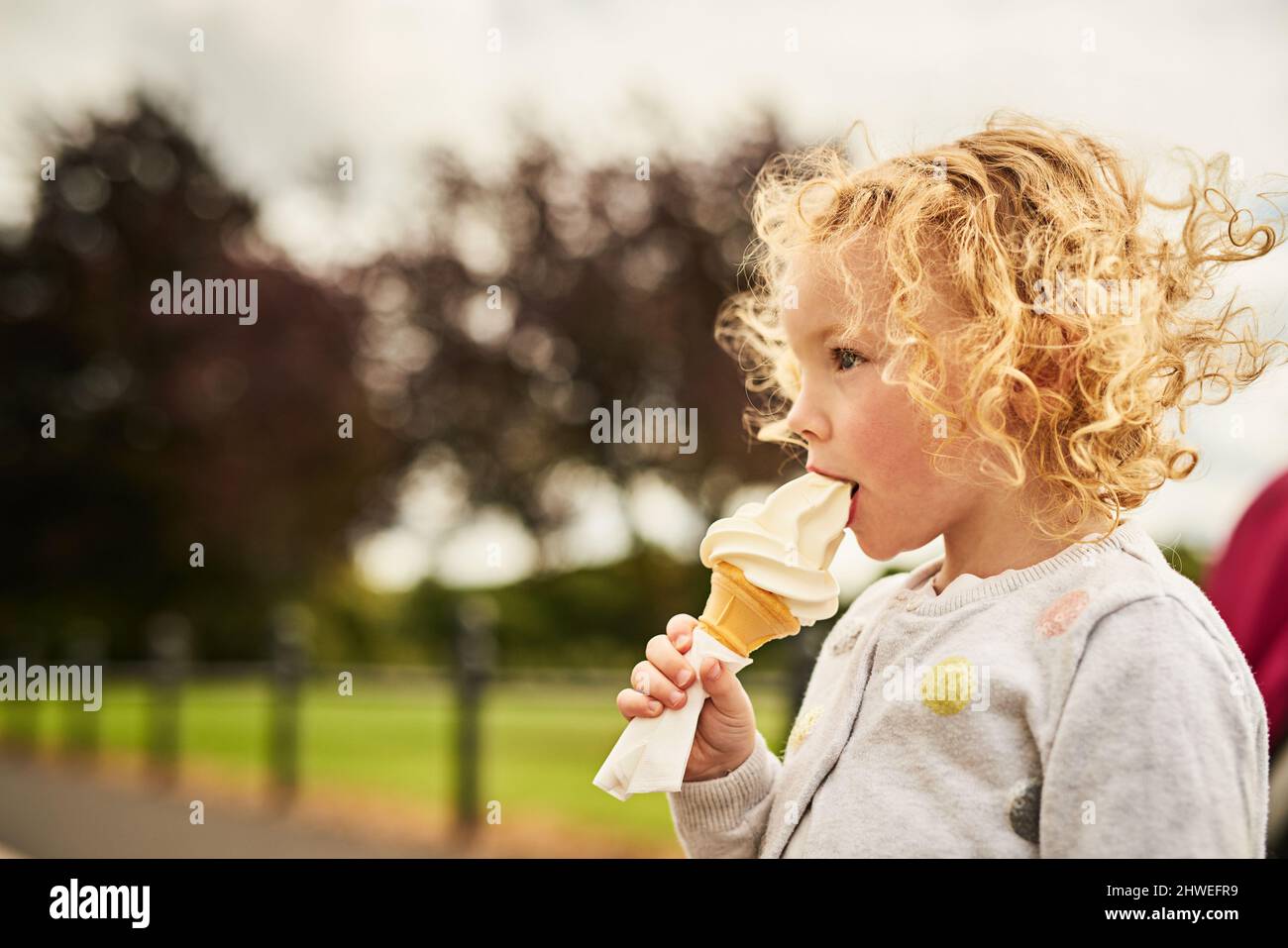 Divertimento e yum vanno bene insieme. Shot di una bambina adorabile che mangia un cono gelato all'aperto. Foto Stock