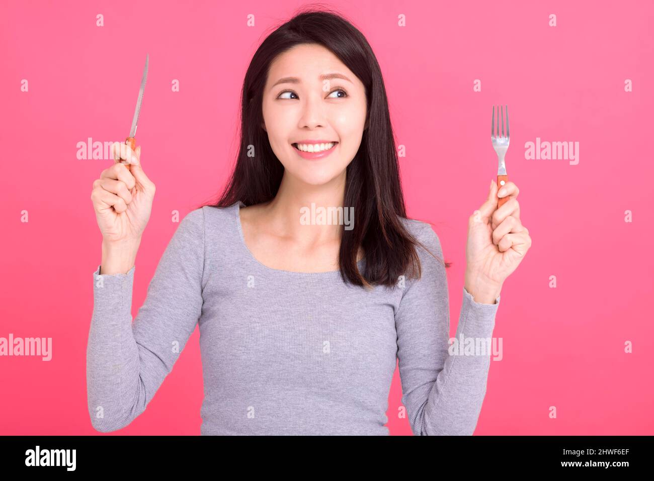 Giovane donna felice tenere coltello forchetta e gustare un pasto gustoso Foto Stock