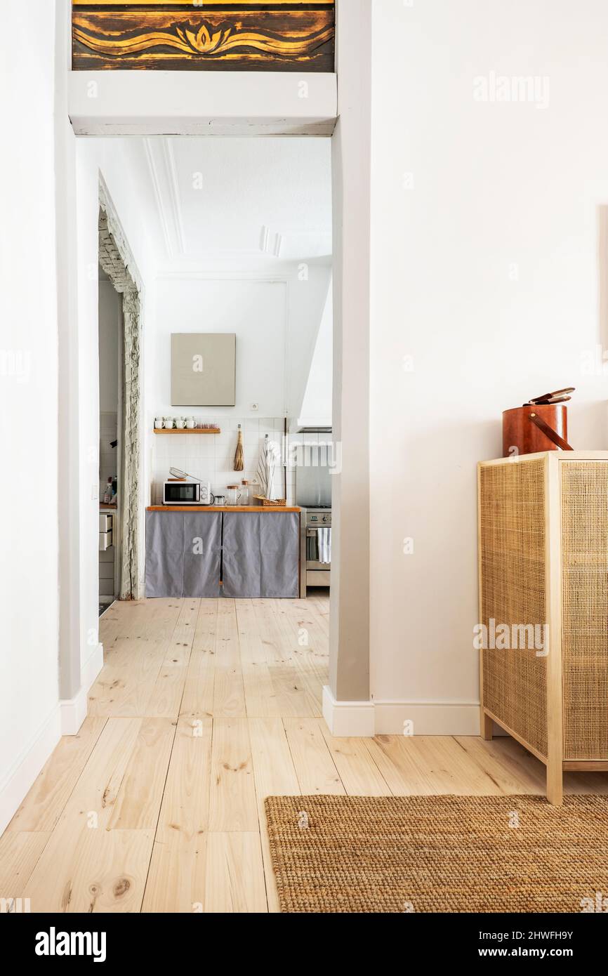 Cucina vista dal soggiorno con mobili in vimini e sogni di pavimenti in legno di pino con grandi assi e tappeto esparto Foto Stock