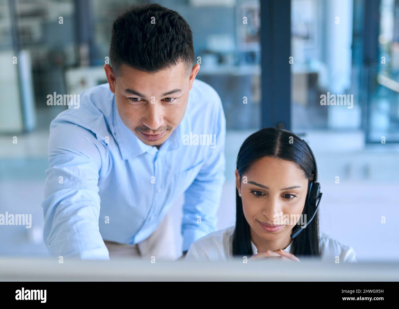 Passare la torcia delle competenze del servizio clienti. Scatto di un giovane che aiuta il suo collega in un moderno call center. Foto Stock