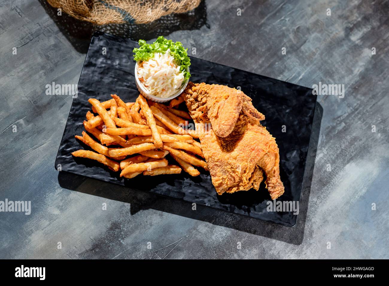 Pollo fritto croccante di primavera (metà) con patatine fritte e bagno mayo in un piatto nero vista dall'alto su sfondo scuro fast food Foto Stock