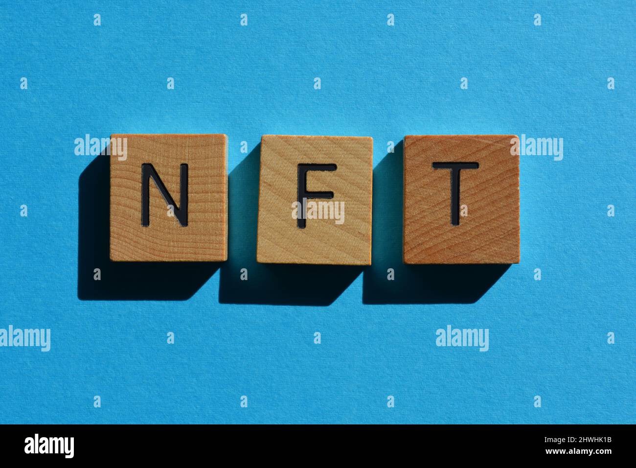 NFT, abbreviazione di token non-fungibile, in lettere in legno su sfondo blu Foto Stock