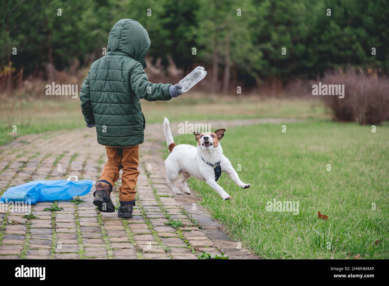 Il bambino gioca con il cane mentre raccoglie i rifiuti di plastica nel parco. La famiglia aggiunge divertimento al lavoro volontario Foto Stock