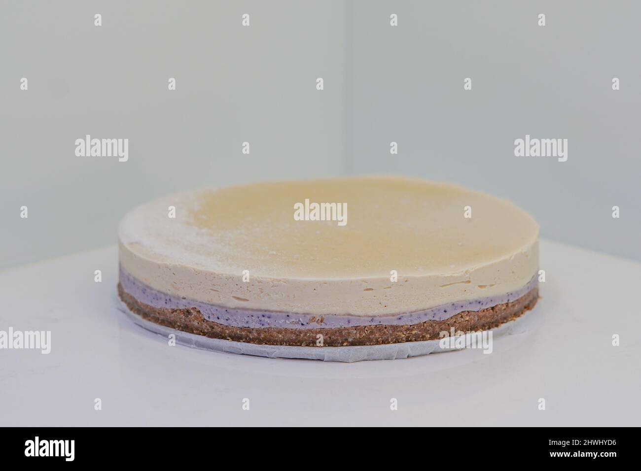 Cheesecake casalinga di stile New york con fondazioni marroni viola mirtillo medio e giallo posto sulla parte superiore del bancone bianco Foto Stock