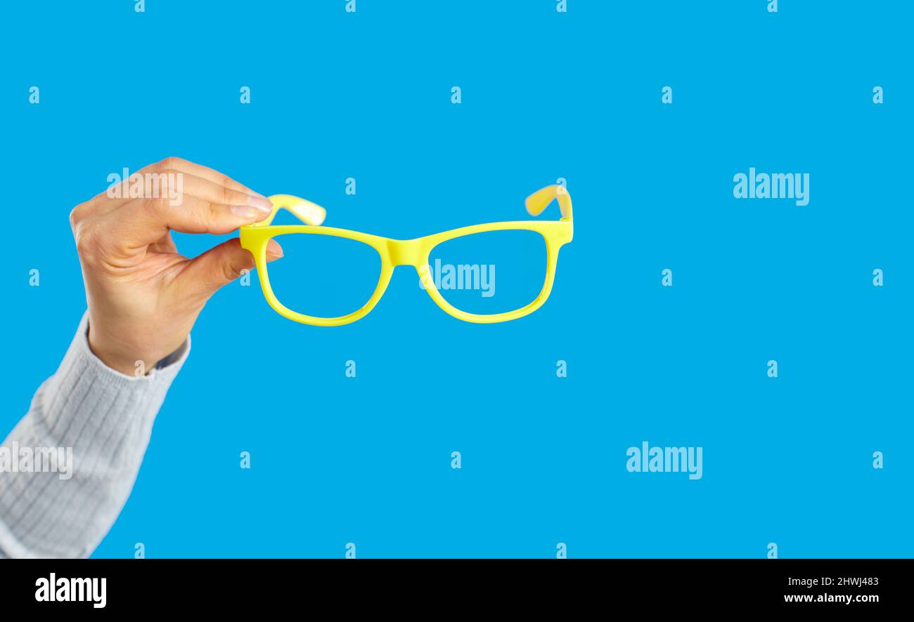 Donna che tiene un paio di occhiali con montatura in plastica gialla su sfondo blu Foto Stock