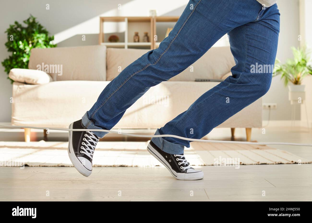 Primo piano di gambe di un uomo sconosciuto che cadono a causa di ciò che inciampa sul cavo di alimentazione a casa. Foto Stock