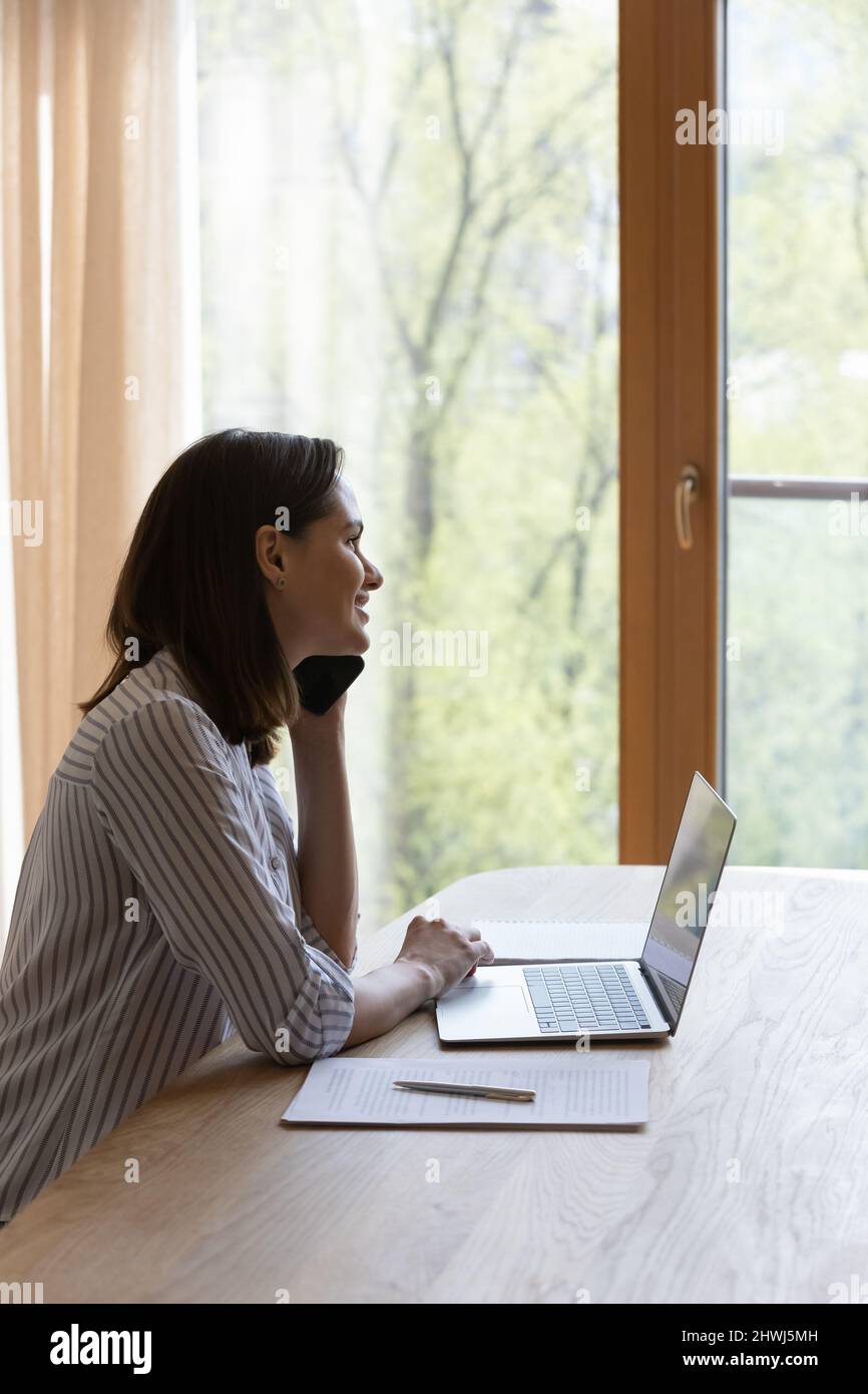 Donna sorridente guarda fuori finestra godere piacevole conversazione sulla phonecall Foto Stock