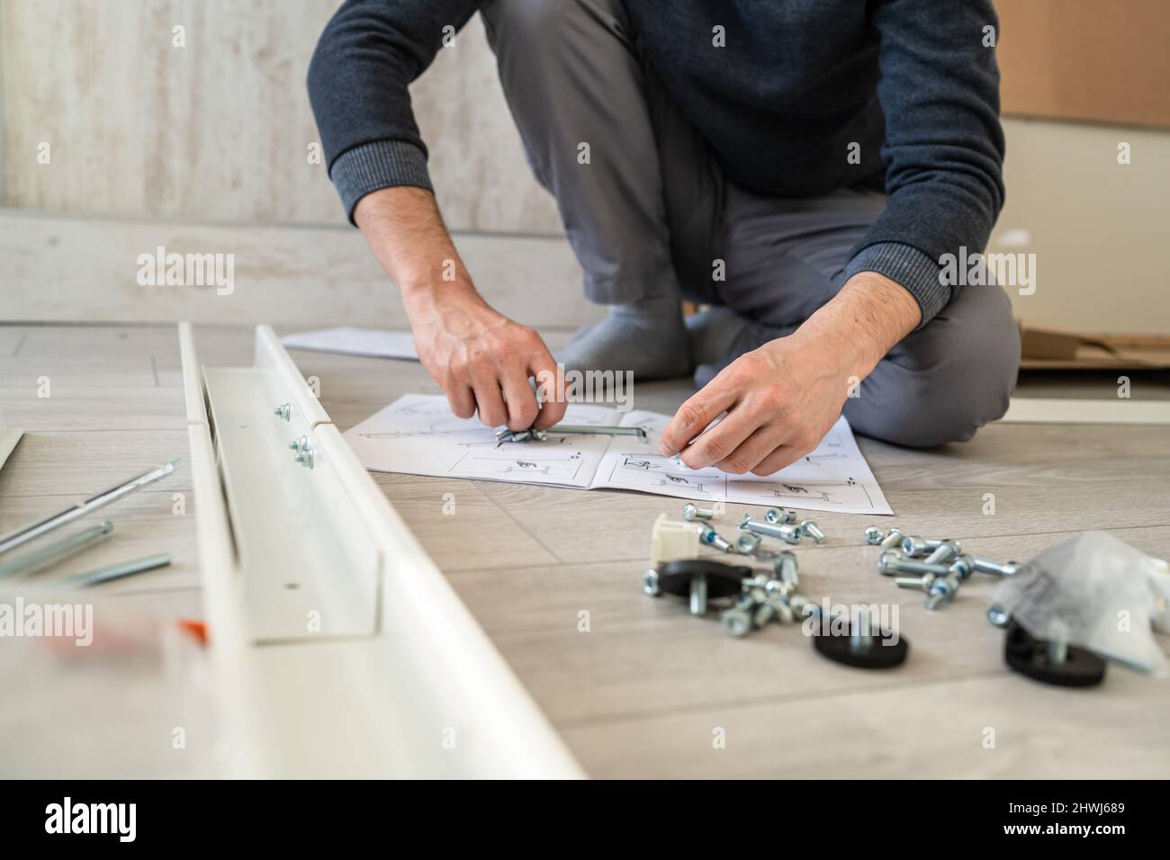 Un uomo sconosciuto maschio caucasico seduto sul pavimento a casa mettendo insieme Self Assembly Mobili diy assemblaggio tenendo parti e istruzioni reali Foto Stock