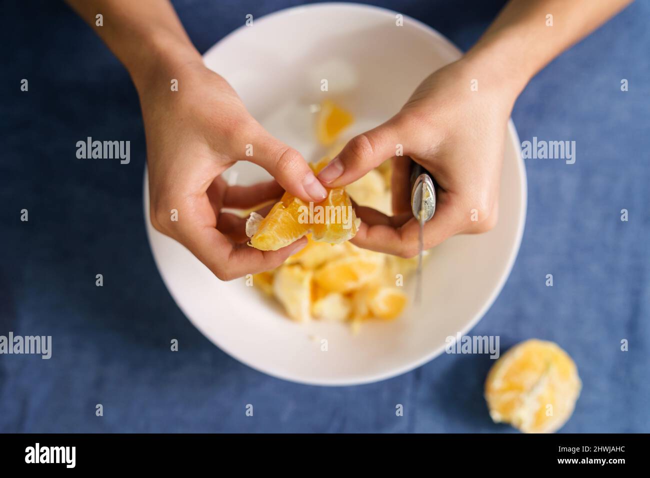Primo piano sulle mani di sconosciuta donna caucasica che separa le fette di arancia sulla ciotola sul tavolo a casa - sano concetto di cibo biologico omemade Foto Stock