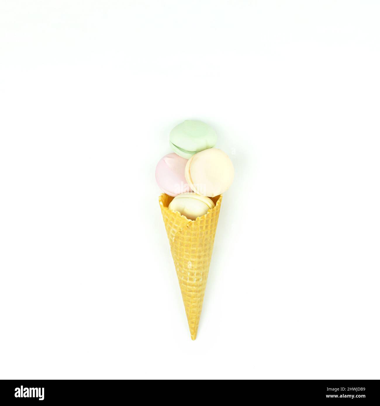 Cono giallo waffle con marshmallow verde, rosa e giallo sembra macaroon su sfondo bianco Foto Stock