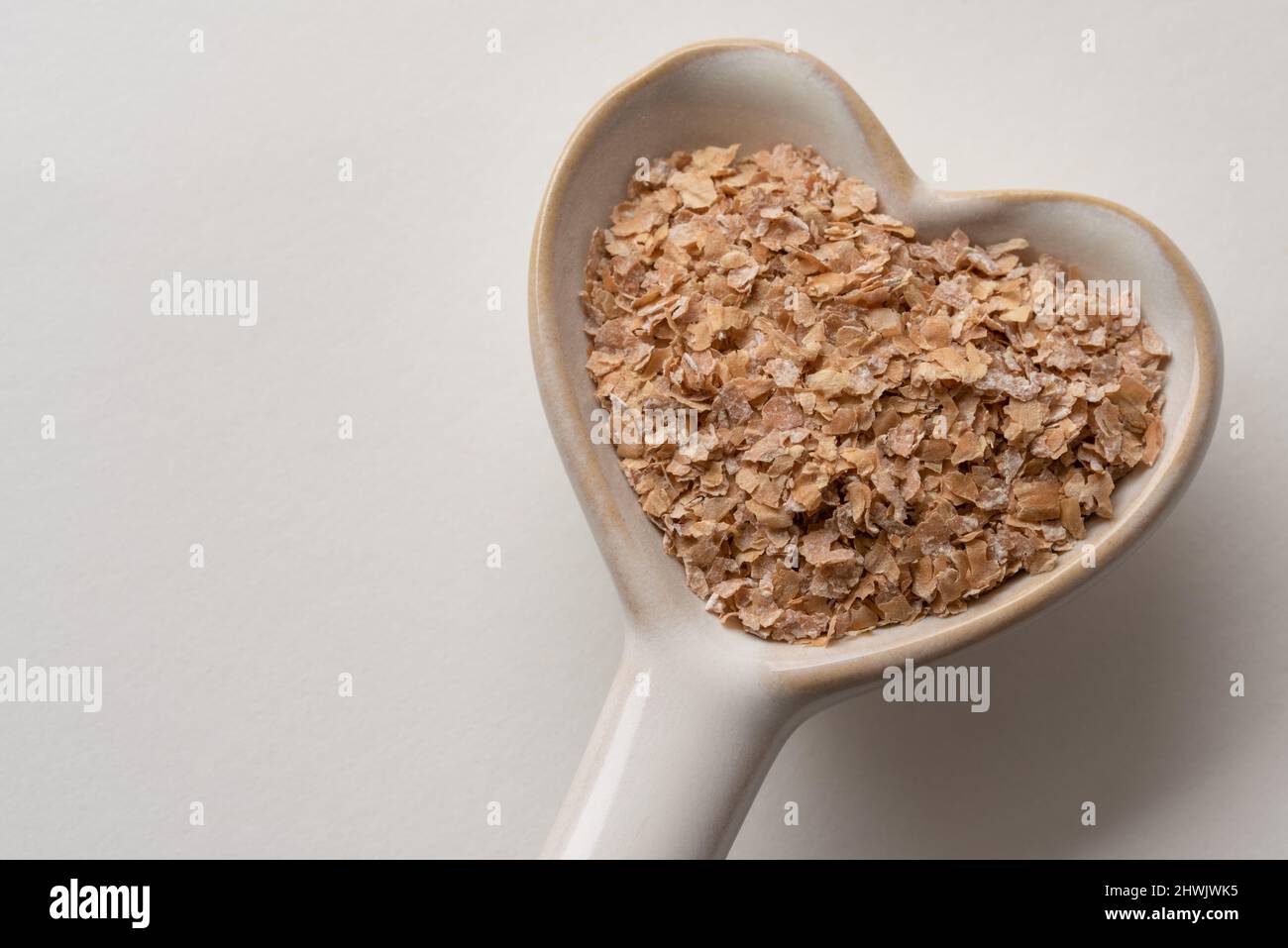 Crusca di grano su un cucchiaio a forma di cuore Foto Stock