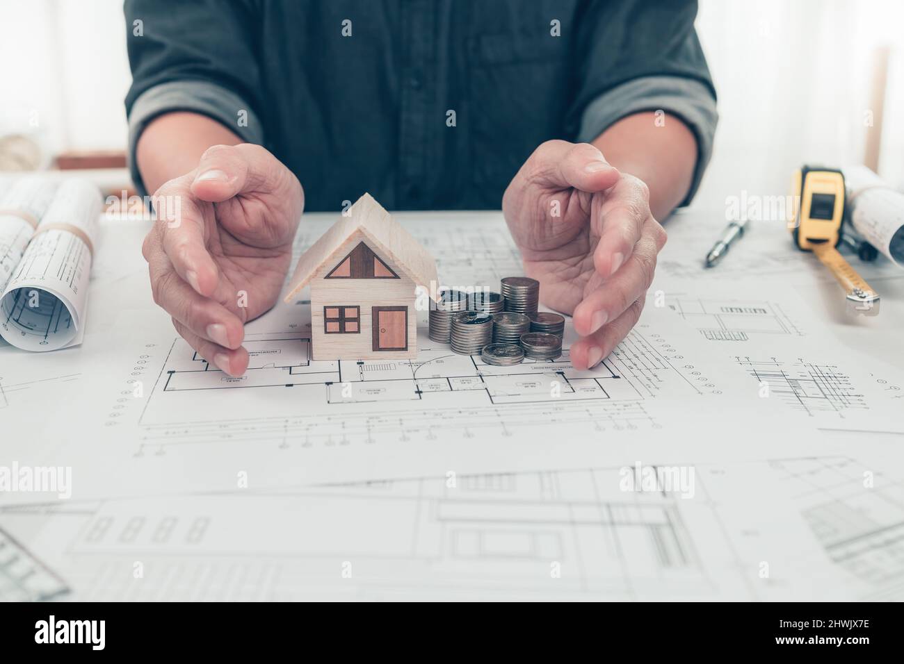 Architetto ingegnere mani protact casa e moneta di denaro su bueprint. Costo Casa progettazione e costruzione concetto. Foto Stock