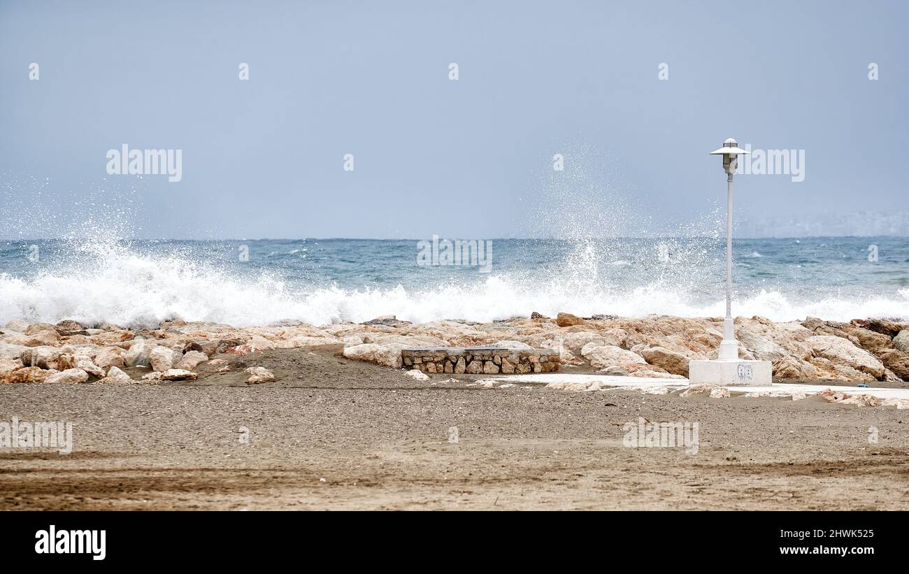 Le onde di mare si infrangono contro un frangiflutti vicino alla spiaggia con un lampione nelle vicinanze Foto Stock