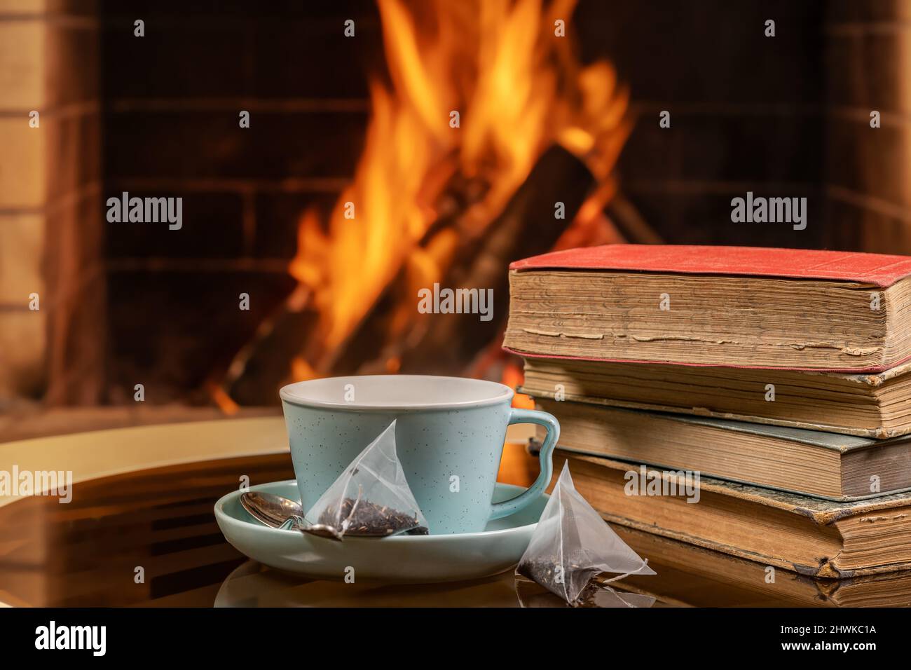 Una tazza di tè e vecchi libri sullo sfondo di un camino in fiamme. Foto Stock