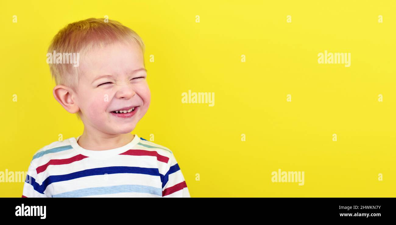 Primo piano Ritratto di un bel ragazzo ridendo. Adorabile bambino piccolo ride su sfondo giallo. Carino biondo ragazzo sorridendo e ridendo. Foto Stock