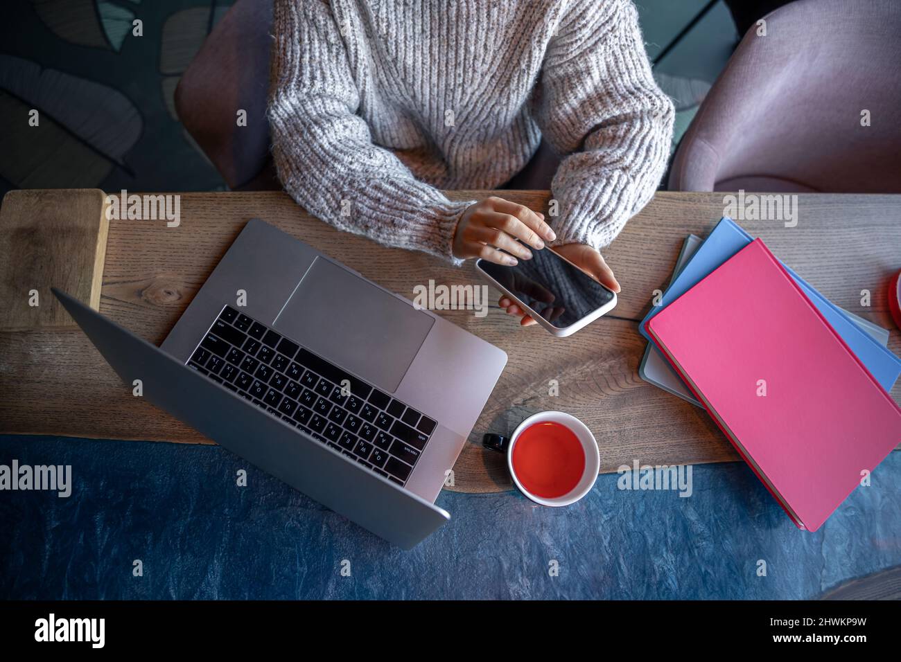 Donna che lavora su un computer portatile in un bar con una tazza di tè, vista dall'alto. Foto Stock