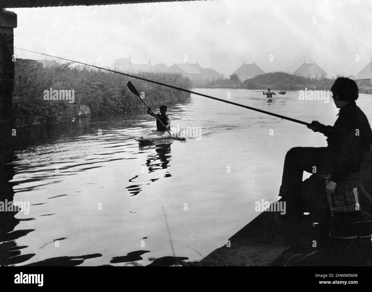 Leeds e Liverpool Canal, domenica 23rd luglio 1972. Due diversi tipi di sport si incontrano faccia a faccia sul Leeds Liverpool Canal, energici canoisti del Lancashire, Cheshire e l'Isola di Man TAVR Association scivolano oltre sedentario pescatori domenicali. I canoisti nella foto stanno competendo nelle prove individuali del tempo della canoa del TAVR, il pescatore solista è un ragazzo desideroso di bagnare una linea. TAVR Territorial e Army Volunteer Reserve Foto Stock
