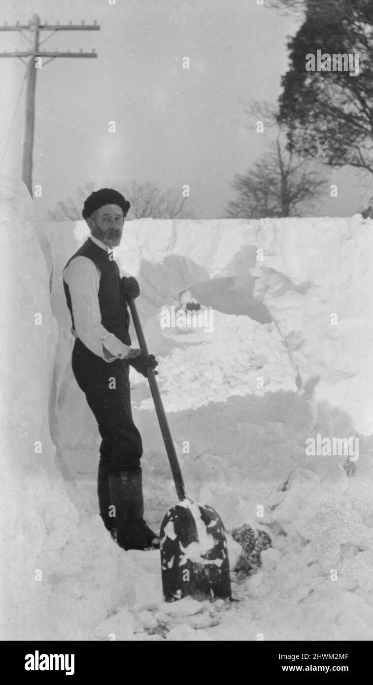 Uomo che spanna la neve che va sopra le sue spalle Foto Stock