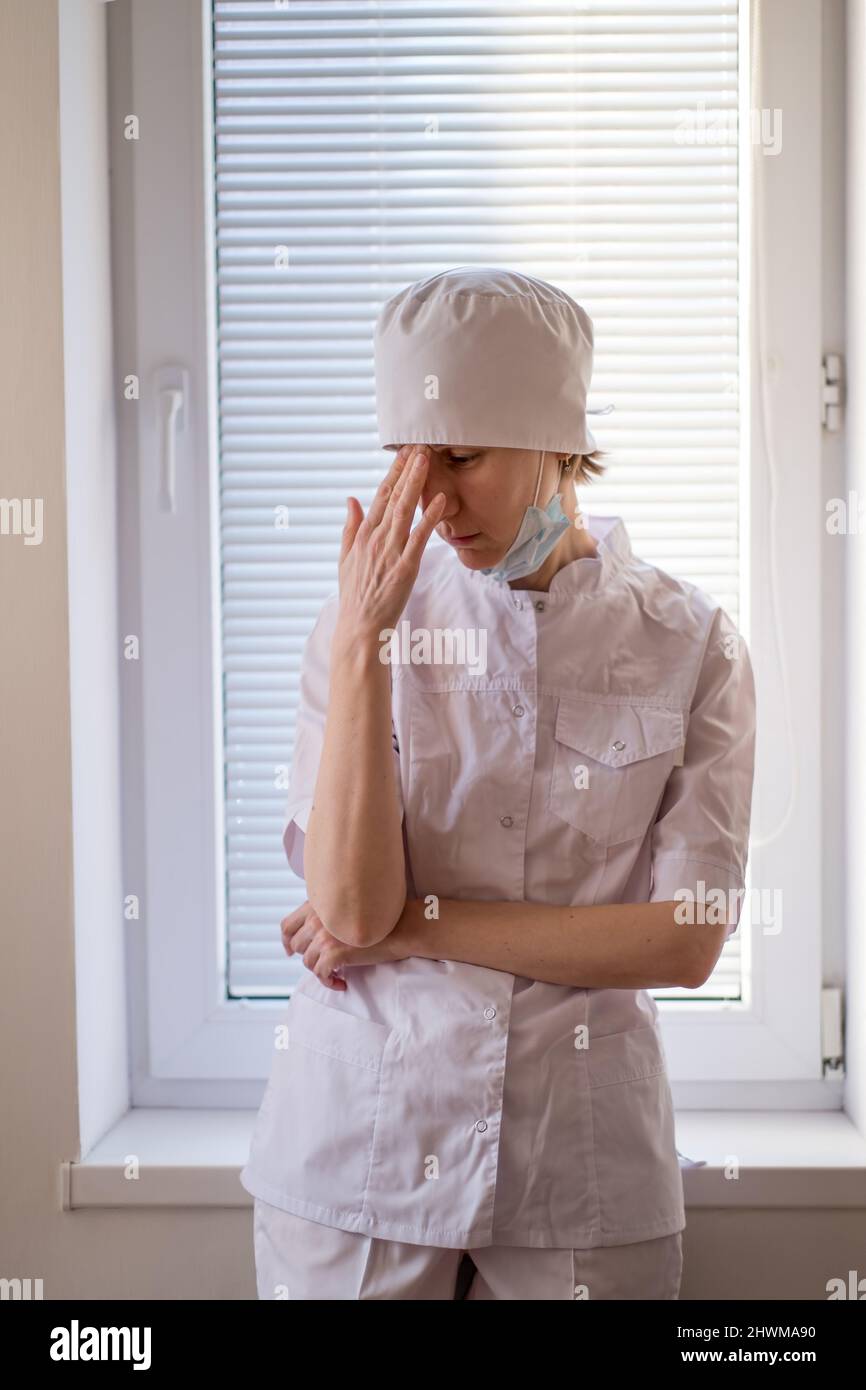 Il medico femminile tocca la fronte pensosamente e si alza alla finestra. Foto Stock
