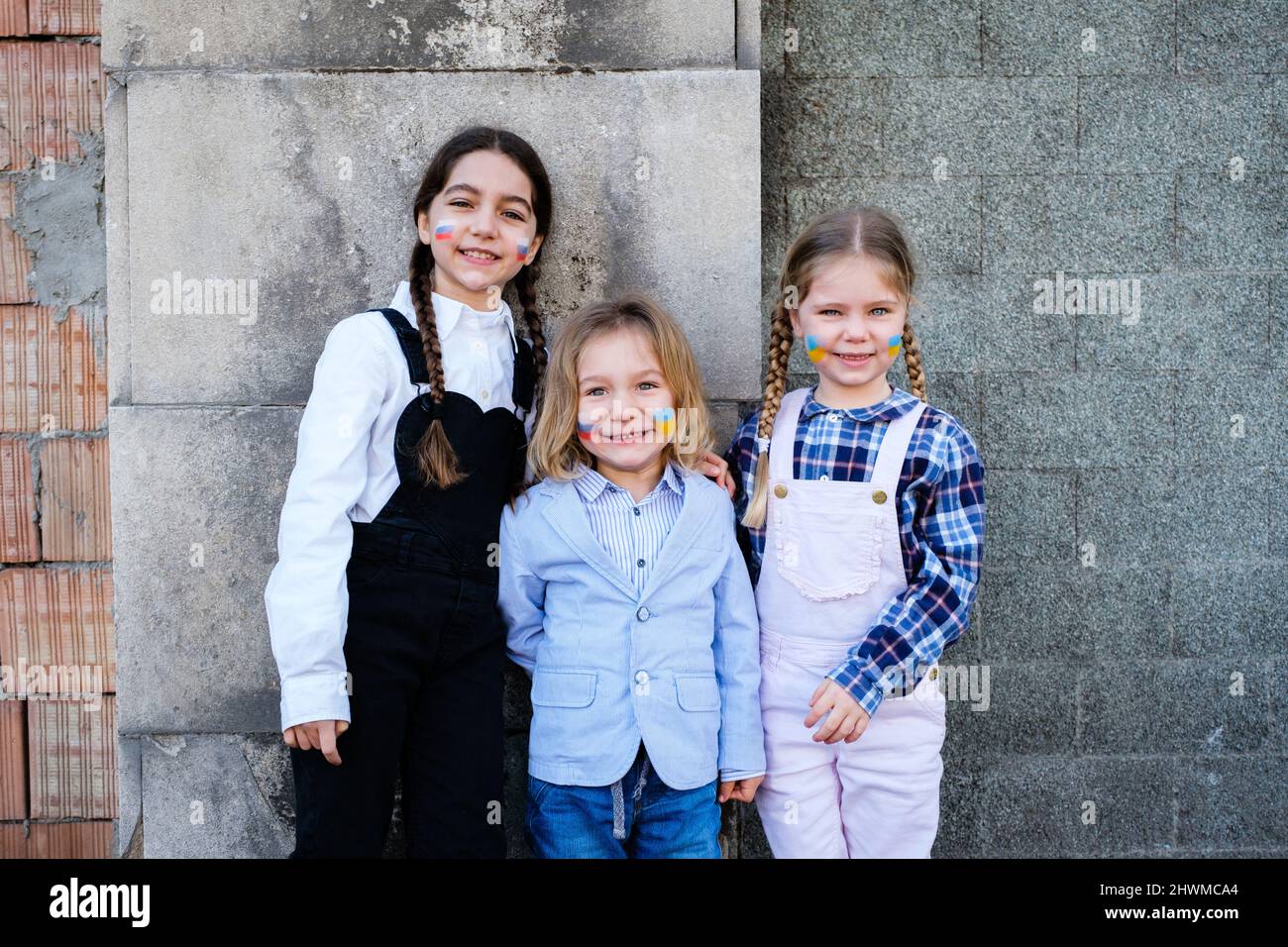 Ritratto di bellissimi tre bambini caucasici che abbracciano bandiere russe e ucraine sui volti. Concetto di pace, fermare la guerra e l'amicizia Foto Stock