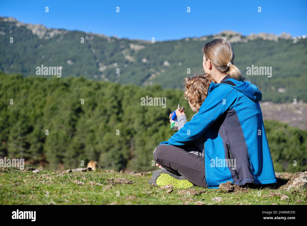 Un bambino adorabile che beve un cartone di latte attraverso una paglia in natura con la madre Foto Stock