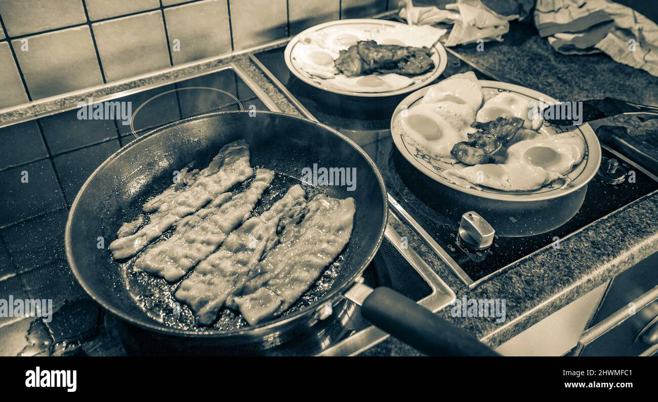 Vecchio quadro bianco e nero di uova fritte e fare uova fritte salsiccia e prosciutto nella padella al mattino. Foto Stock