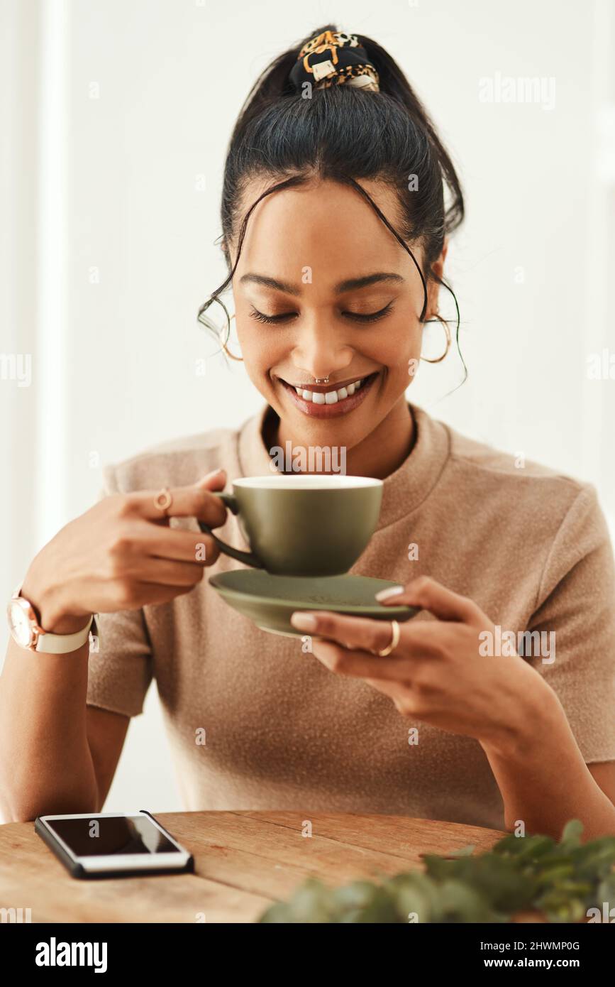 Questo buon umore è stato sponsorizzato dal caffè. Scatto corto di una giovane donna attraente seduta da sola nella sua casa e godendo una tazza di caffè. Foto Stock