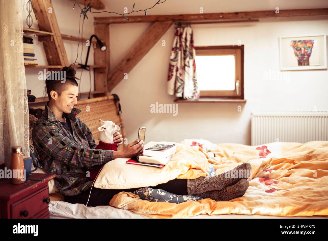 La donna mista si siede a letto con cane e video chat sul telefono Foto Stock