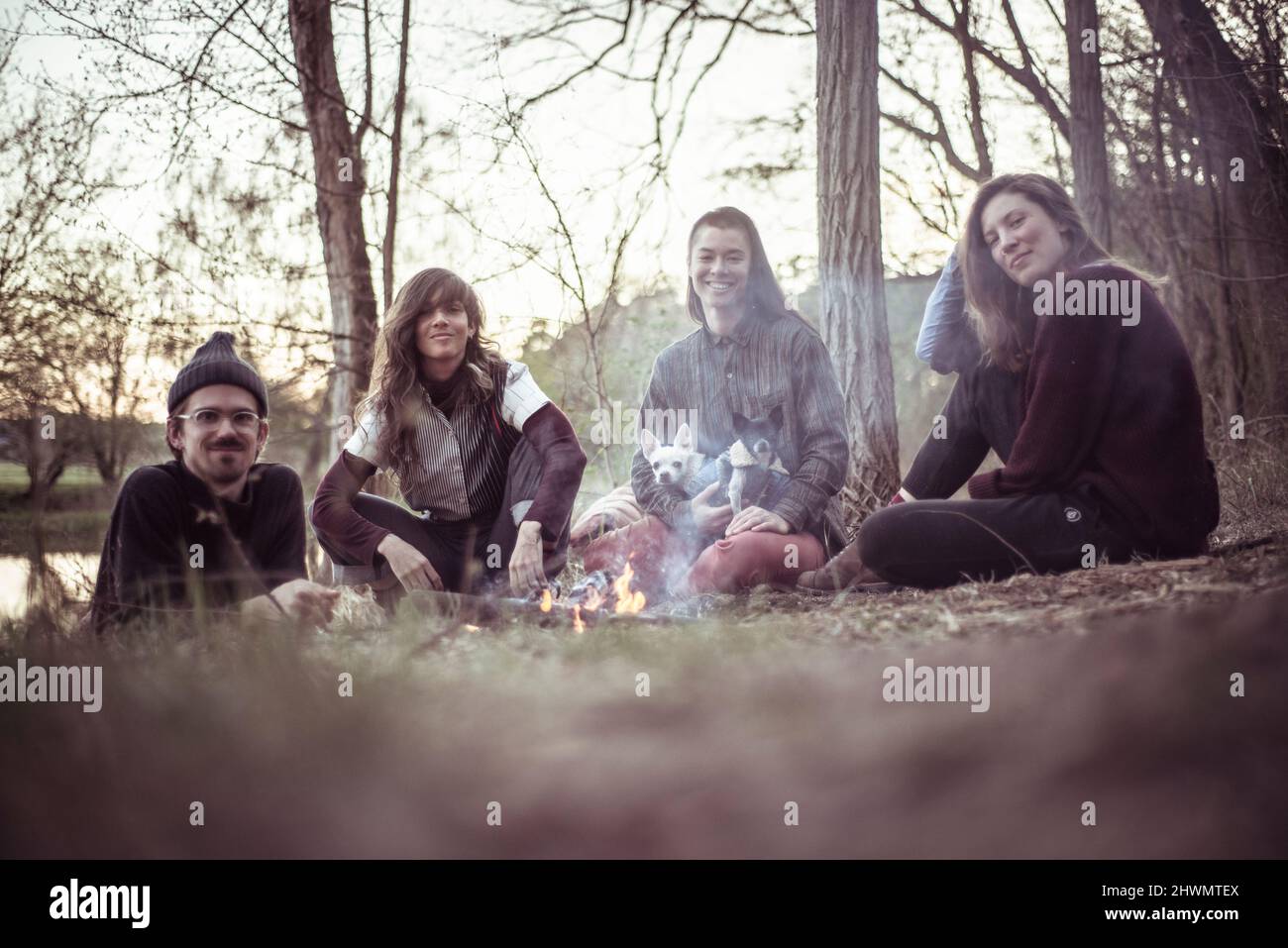 gli amici alternativi si siedono intorno al fuoco del campo con i cani piccoli Foto Stock