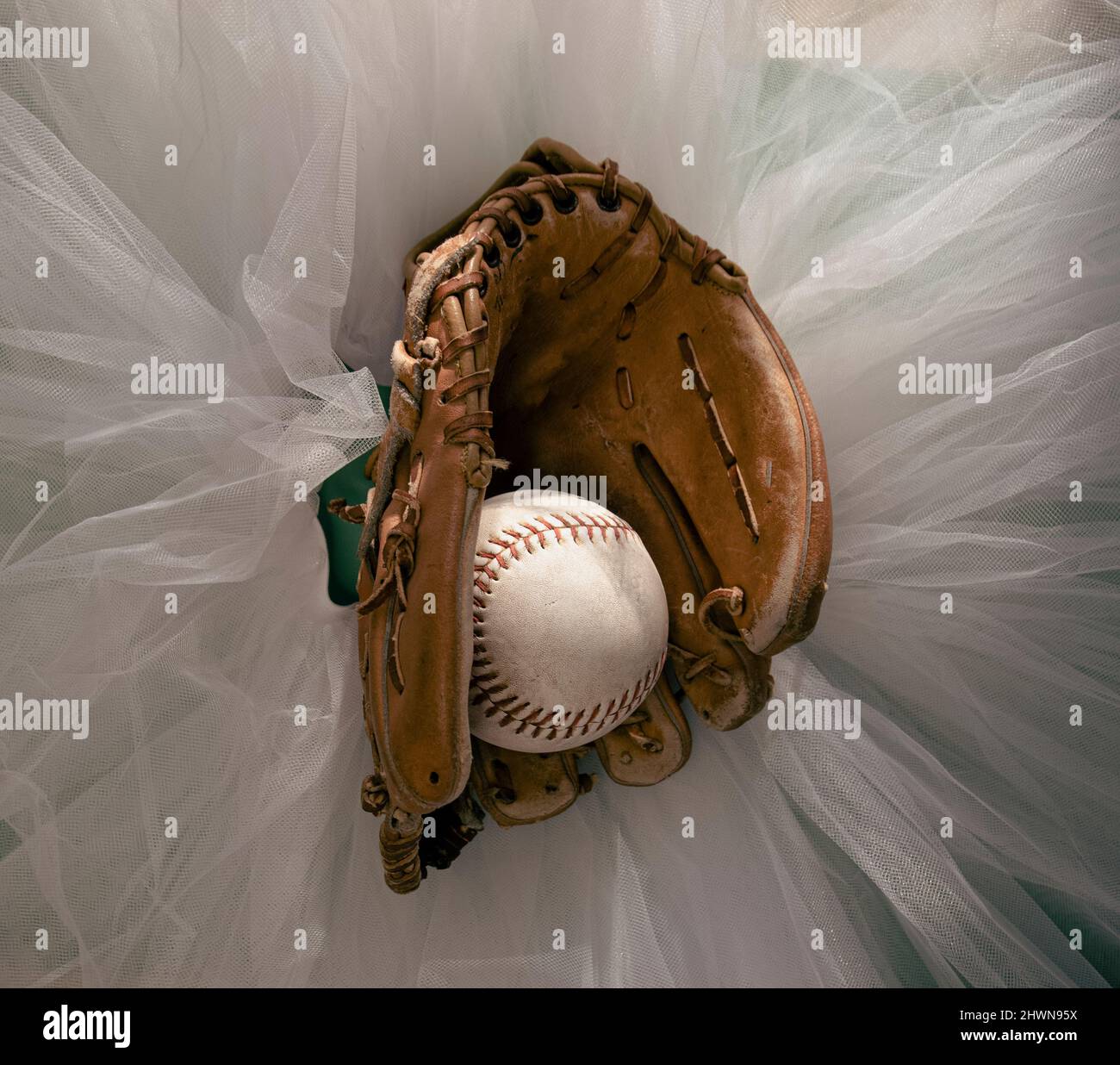 Guanto da baseball con softball a metà, seduto in cima a un tutu balletto bianco. Foto Stock