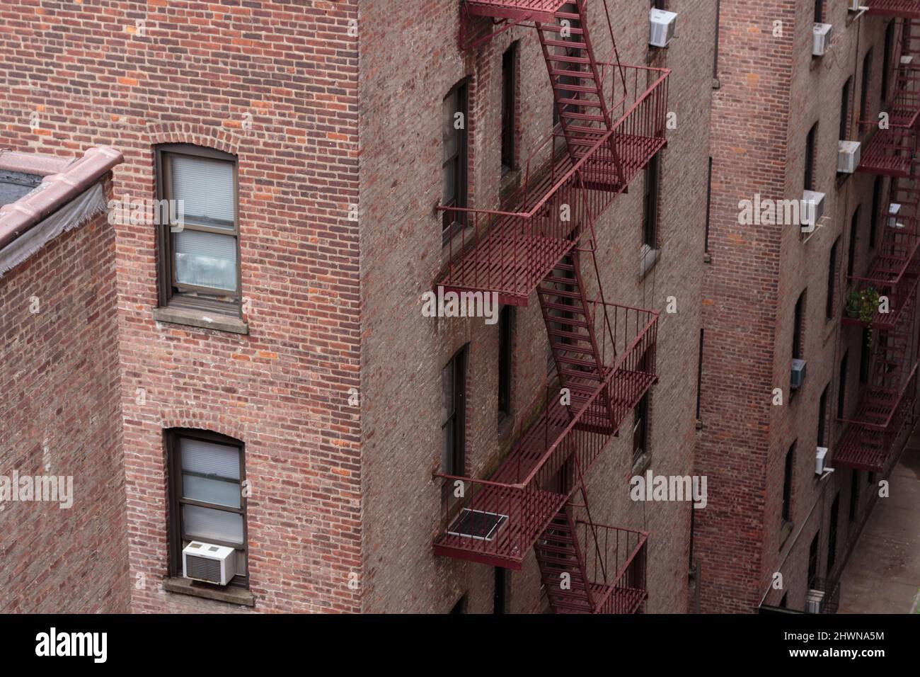 retro di edifici di appartamenti in mattoni rossi dall'aspetto generico, non descritti, con fughe di fuoco e finestre con aria condizionata Foto Stock