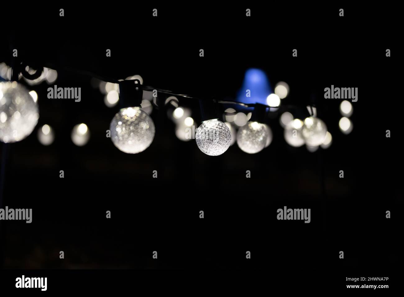 una serie di lampadine decorative rotonde su sfondo nero con un raggio di luce blu sullo sfondo, si dissipano in effetto bokeh con spazio copia Foto Stock