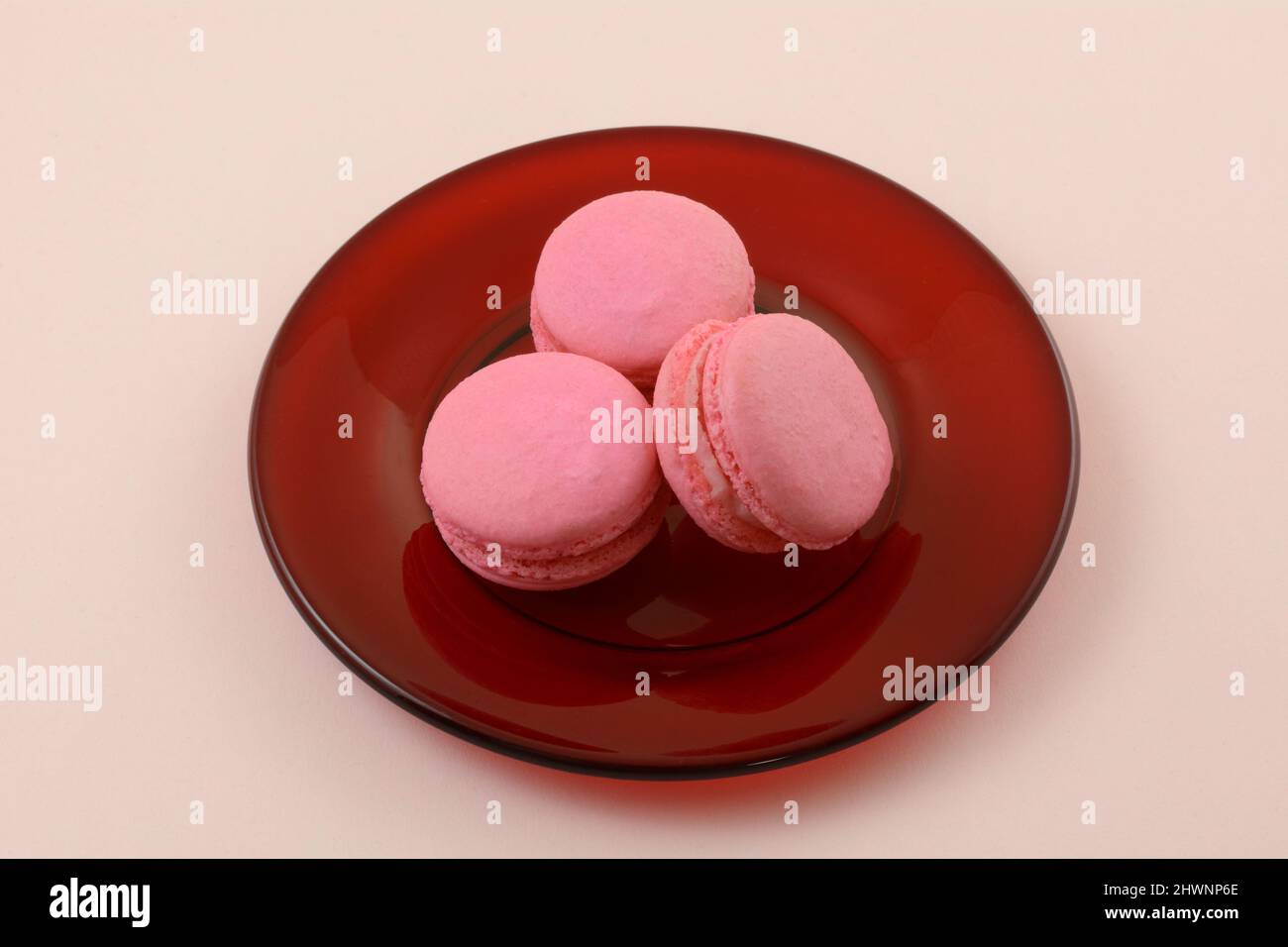 Biscotti di macaron francese di lampone rosa su un piatto di vetro rosso su sfondo rosa Foto Stock