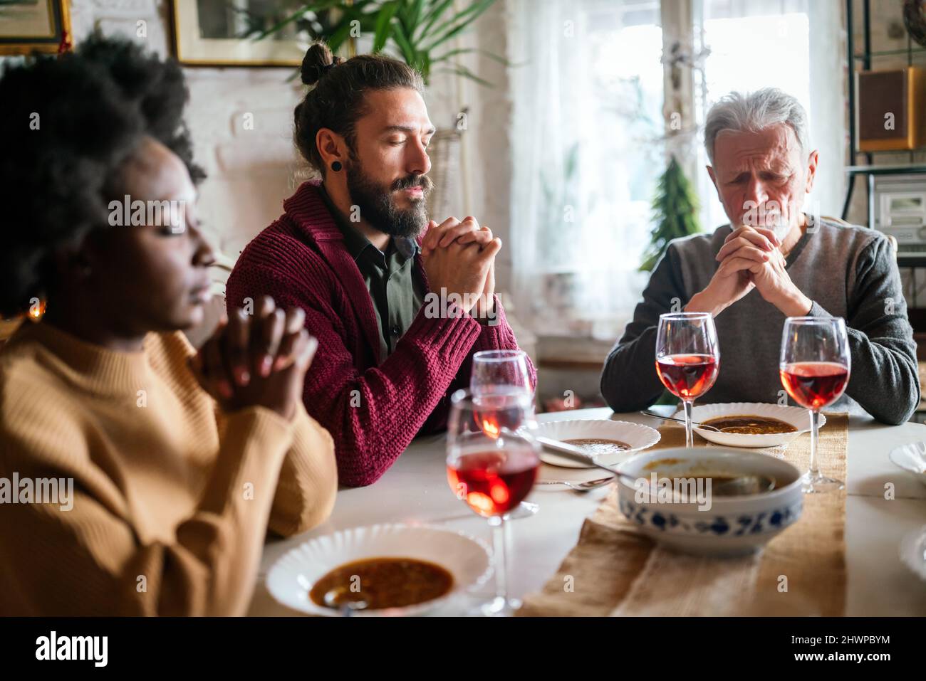 Famiglia e concetto religioso. Gruppo di persone multietniche con cibo che prega prima del pasto Foto Stock