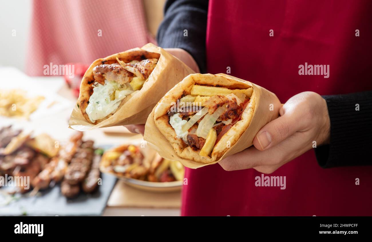 Gyro pita Shawarma. Cibo greco, affettati, patate, pomodoro e tzatziki, carta in mano maschile, sfondo cucina, vista ravvicinata. Foto Stock